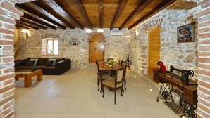 Ein rustikales Interieur mit Steinwänden, einer Holzbalkendecke, einem Esstisch mit Stühlen, einer Couch und einer Nähmaschine.