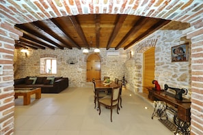 A rustic interior with stone walls, a wooden ceiling, a dining table with chairs, a sofa, and a sewing machine. - Villa Gland with Pool and Whirlpool (Nin)