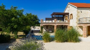 Ein Steinhaus mit Pool, umgeben von viel Grün und einem klaren Himmel.