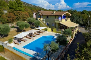 A two-story building with a swimming pool, outdoor seating, and a hillside backdrop. - Villa Paulina with Heated Pool (Starigrad)