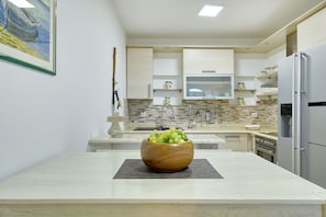 A modern kitchen with a marble countertop, a wooden bowl of fruit, and built-in appliances. - Villa Paulina with Heated Pool (Starigrad)