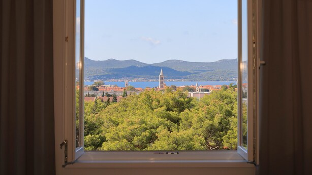 A window view of a cityscape with mountains, a lake, and a church tower.