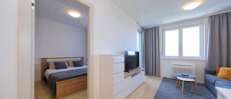 Moderni hotellihuone, jossa on sänky, televisio, sohva ja pieni pöytä.