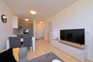 A modern living room with a flat-screen TV, a dining area with chairs and a table, and a kitchen in the background. - Apartment Kostela with Balcony and City View (Zadar)