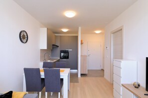 A compact kitchen with modern appliances, a dining area with chairs, and a hallway leading to a door. - Apartment Kostela with Balcony and City View (Zadar)