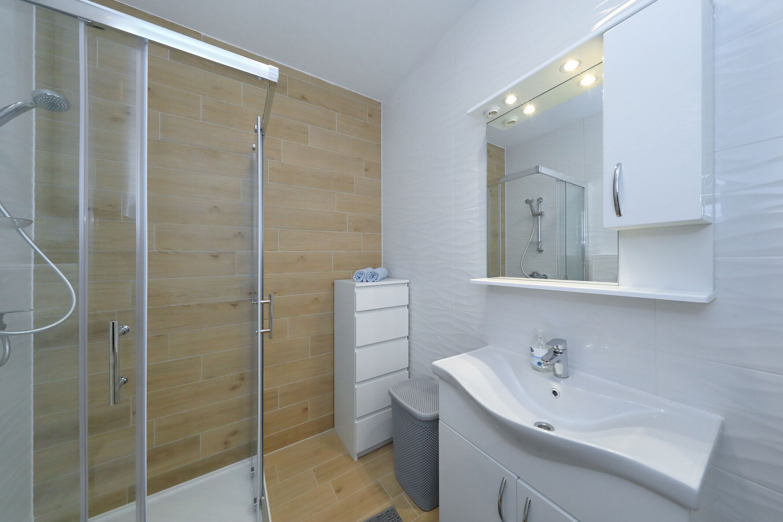 A modern bathroom with a glass shower enclosure, a white sink, and a mirror above the sink.