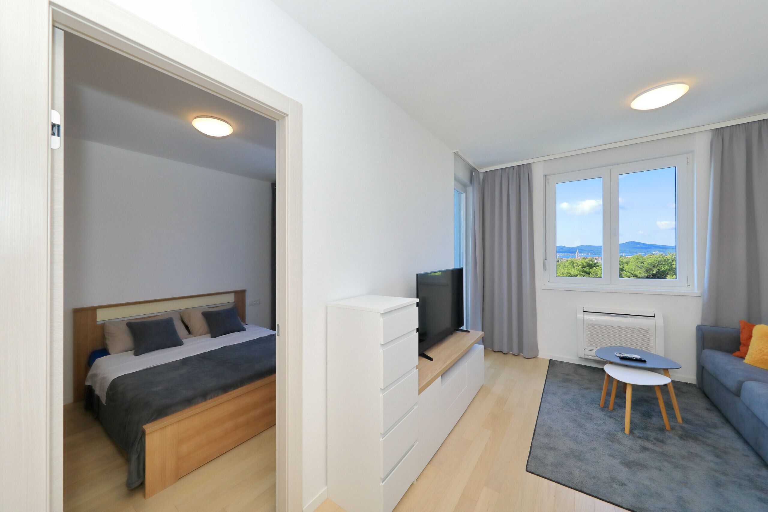 A modern bedroom with a bed, a TV on a stand, a small table, and a sofa.