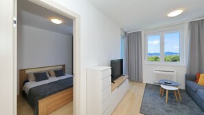 A modern bedroom with a bed, a TV on a stand, a small table, and a sofa.
