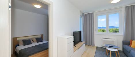 A modern bedroom with a bed, a TV on a stand, a small table, and a sofa.