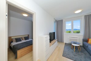 A modern bedroom with a bed, a TV on a stand, a small table, and a sofa. - Apartment Kostela with Balcony and City View (Zadar)