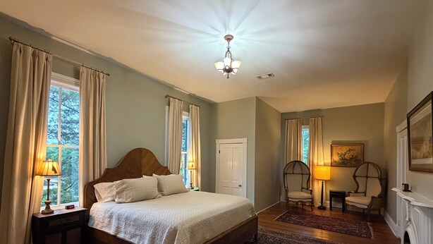 Quarto com uma cama grande, duas mesas de cabeceira com luminárias, uma poltrona, lareira e janela com cortinas.
