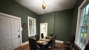 Uma sala de jantar com uma mesa posta para seis pessoas, rodeada por cadeiras, um tapete estampado e um candelabro.
