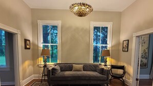 Quarto com sofá, duas luminárias, tapete e duas janelas com vista para árvores.