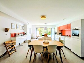 A modern kitchen with white cabinets, a dining table with chairs, and a view to the outside. - Casa Alpilles, Saint-Remy-de-Provence (Saint-Rémy-de-Provence)