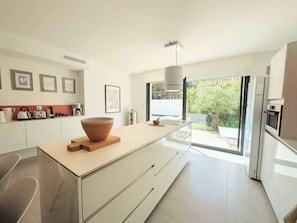 A modern kitchen with a central island, white cabinetry, and a large window offering a view of greenery. - Casa Alpilles, Saint-Remy-de-Provence (Saint-Rémy-de-Provence)