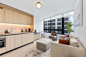 A modern kitchen with a central island, a dining area with a chair, a sofa with cushions, and a large window with a view. - Skyline Pool & Spa Miami (Miami)