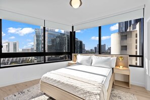 A modern bedroom with a large bed, a nightstand, a wall-mounted lamp, and a city view through large windows. - Skyline Pool & Spa Miami (Miami)