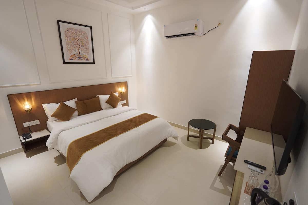Habitación de hotel con cama, mesita de noche, aire acondicionado instalado en la pared y una pequeña mesa con una silla.