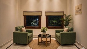 Una habitación con dos sillones verdes, una mesa redonda pequeña con una planta y dos ventanas con persianas.