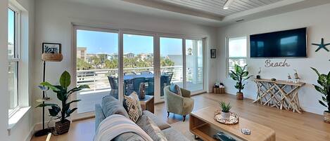 A spacious living room with a large sofa, a coffee table, and a TV mounted on the wall.