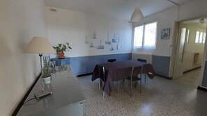 Ein Zimmer mit Tisch, Stühlen, einer Lampe, einer Topfpflanze und einer Heizung.
