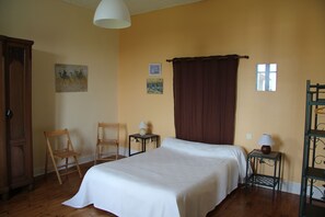 Ein Schlafzimmer mit einem Bett, zwei Stühlen, einem Nachttisch, einer Lampe und einem Fenster.