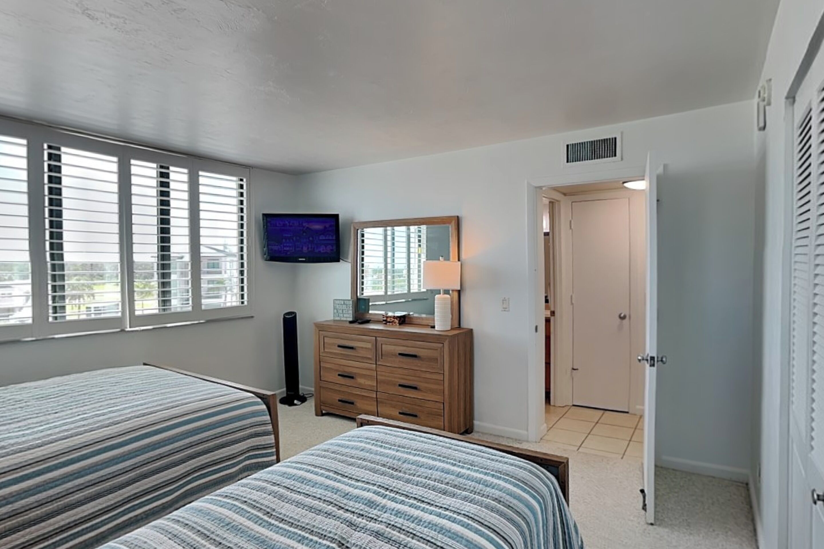 Une chambre avec deux lits, une commode, un téléviseur et une porte donnant sur une autre pièce.