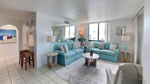 Una sala de estar con un sofá azul, una mesita redonda, un tapete estampado y una silla.