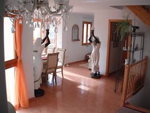 A dining area with a chandelier, a dining table with chairs, a staircase, and a plant on a shelf. - Serenity - pool, mountains and incredible views, near the Relleu footbridge. (Relleu)