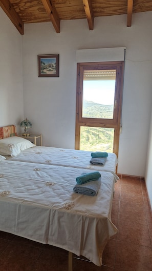 A bedroom with two beds, a nightstand, a lamp, a framed picture, and a window with a view. - Serenity - pool, mountains and incredible views, near the Relleu footbridge. (Relleu)