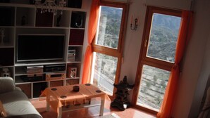 A living room with a TV, shelves, a table, and a view through windows. - Serenity - pool, mountains and incredible views, near the Relleu footbridge. (Relleu)