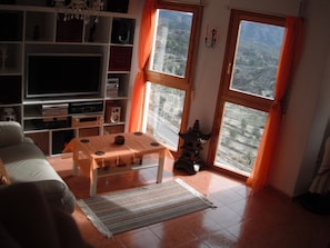A living room with a TV, shelves, a table, and a view through windows. - Serenity - pool, mountains and incredible views, near the Relleu footbridge. (Relleu)