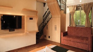Een woonkamer met een bank, een flatscreen televisie aan de wand, een trap en houten vloeren.