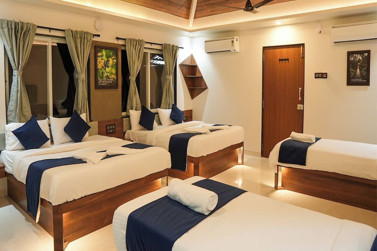 Habitación de hotel con tres camas, techo de madera y una puerta con un pequeño estante encima.