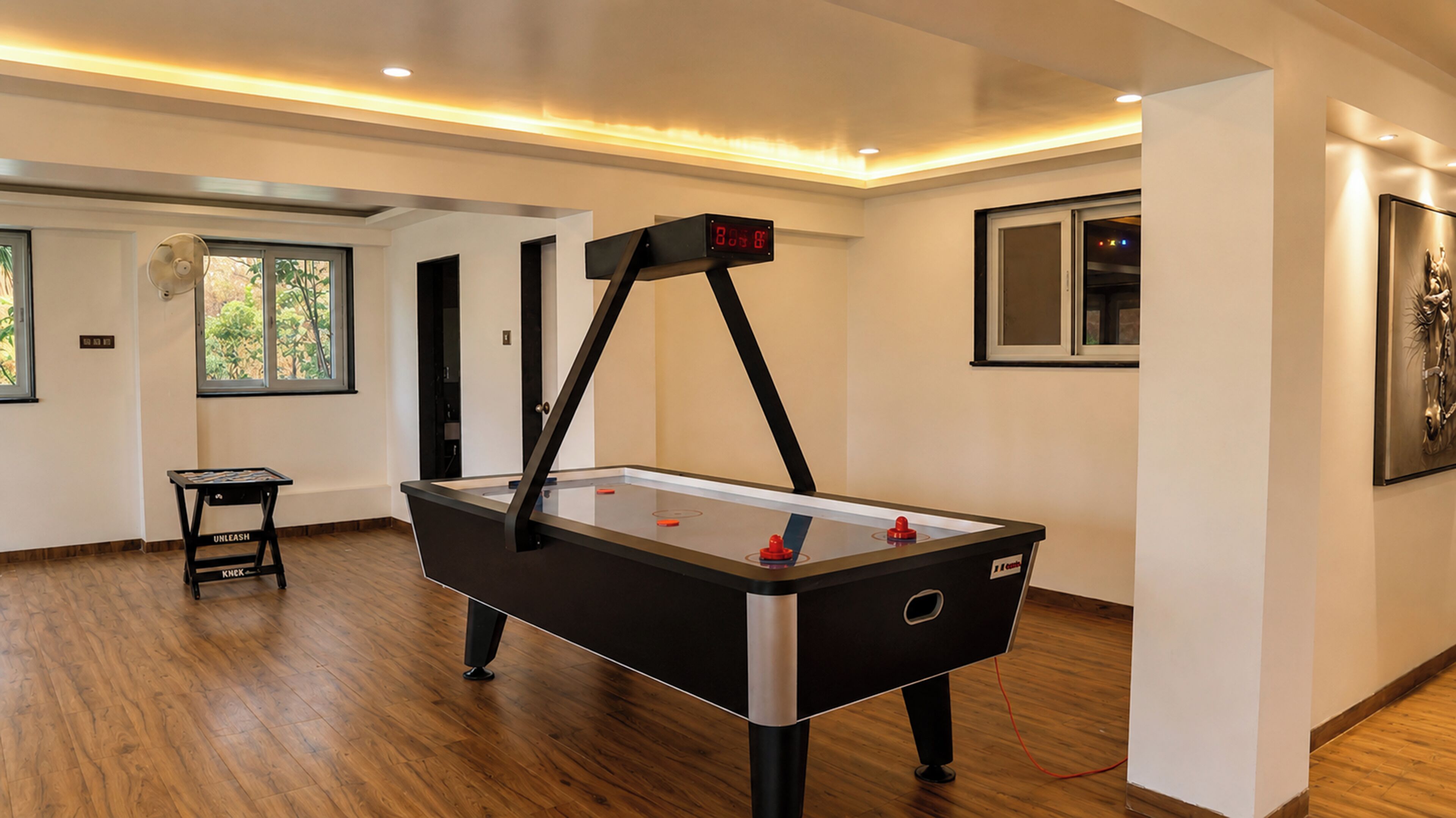 A modern indoor pool table with a digital scoreboard, wooden flooring, and a framed artwork on the wall.