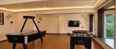 Een kamer met een pooltafel, een tafelvoetbalspel en een aan de muur bevestigde televisie.