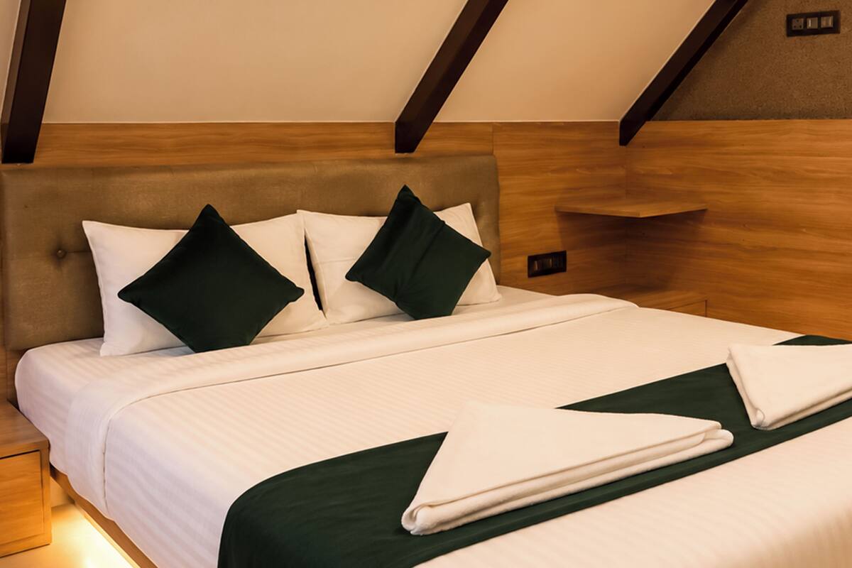 Una cama bien tendida con cabecera, almohadas y una manta verde.