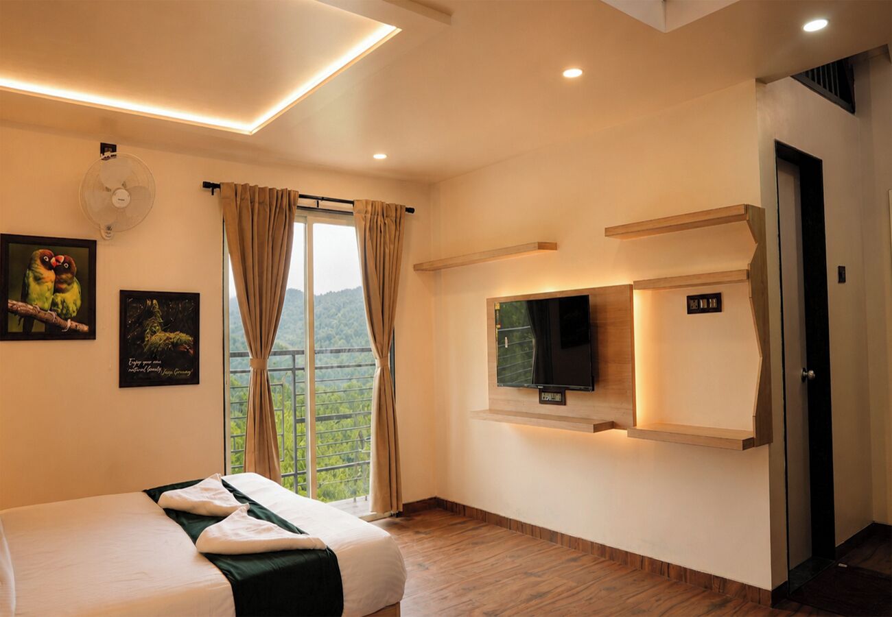 Habitación de hotel con cama, televisor montado en la pared, ventana con cortinas y vistas al exterior.