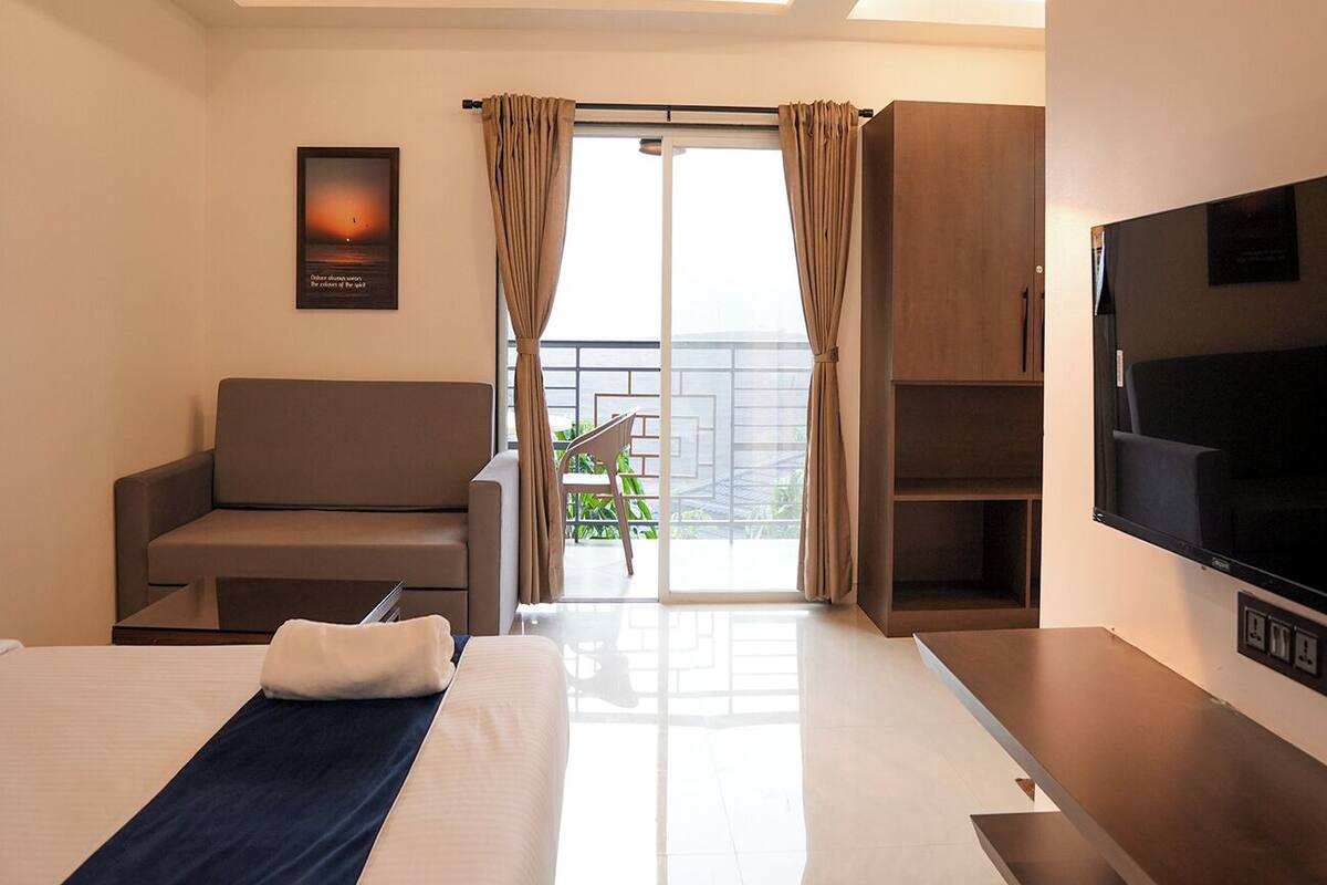Habitación de hotel con cama, sofá, televisor y balcón con cortinas, además de un cartel en la pared.