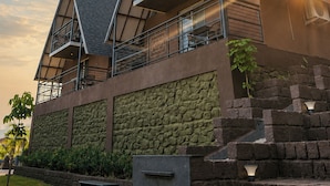 Een modern gebouw met een opvallend dak in driehoeksvorm, een gevel van natuursteen en een balkon met een metalen hekwerk.