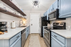 Cocina compacta con encimera blanca, electrodomésticos de acero inoxidable y armarios azul claro.