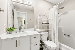 Un baño moderno con lavamanos, espejo, inodoro y ducha blancos.