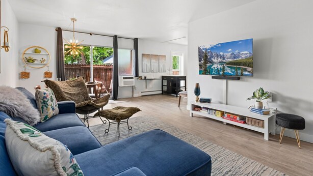 Een moderne woonkamer met een blauwe bank, een eethoek, een keuken en een grote televisie aan de muur.