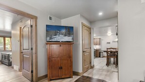 A hallway with wooden flooring, a television on a cabinet, and a dining area with a table and chairs. - Park City 2BR Condo, Jupiter Inn, Community Hot Tub, Sleeps 6 (Park City)