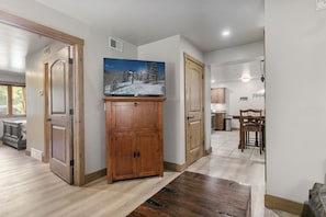 A hallway with wooden flooring, a television on a cabinet, and a dining area with a table and chairs. - Park City 2BR Condo, Jupiter Inn, Community Hot Tub, Sleeps 6 (Park City)