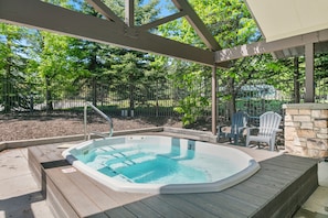 A hot tub with a wooden deck, surrounded by a covered patio area with chairs and a stone wall. - Park City 2BR Condo, Jupiter Inn, Community Hot Tub, Sleeps 6 (Park City)