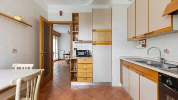 A kitchen with wooden cabinets, a microwave, a sink, and a dining area with a chair.