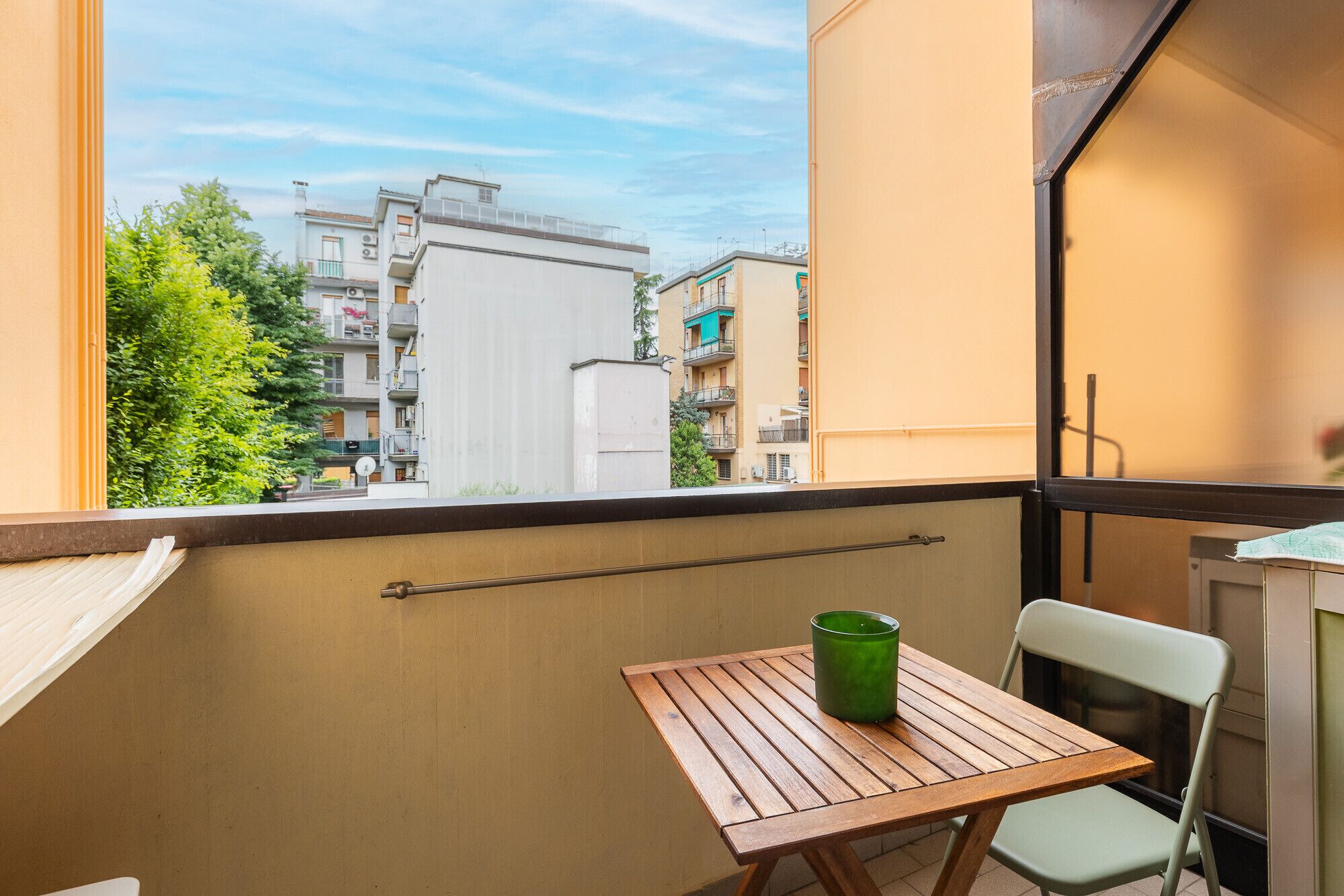 A balcony with a wooden table and a green vase, overlooking a residential area.