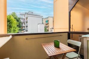 Ein Balkon mit Holztisch und grüner Vase, mit Blick auf ein Wohngebiet.