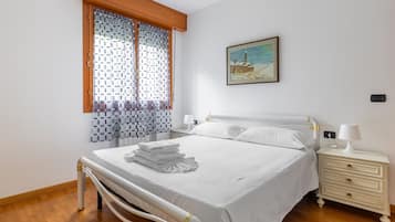 A bedroom with a bed, a nightstand, a lamp, a window with curtains, and a painting on the wall.